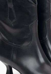 Czarne skórzane botki za kostkę o gładkim, błyszczącym wykończeniu, z trójkątnym wycięciem i dopasowanym krojem. Wysoki, zaokrąglony obcas dodaje elegancji.