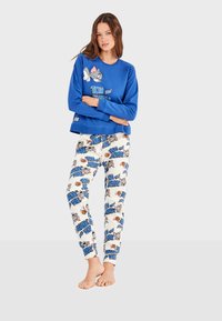 Sweat-shirt bleu avec un graphique "Tom et Jerry" ; pantalon de pyjama blanc à motifs présentant des personnages de dessin animé et du texte. Tissu doux et décontracté.