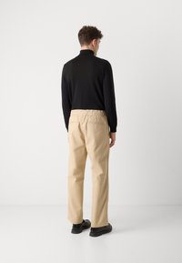 Pantalons beiges avec ceinture élastique, haut noir à manches longues, portés avec des chaussures noires. Texture lisse et coupe décontractée, design minimaliste.