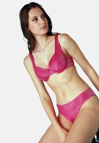 Set di lingerie rosa realizzato in un materiale lucido e testurizzato. Il reggiseno ha ferretti e spalline larghe; le mutandine presentano un design a vita alta.