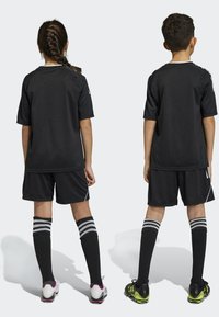 Schwarzes Sporttrikot und Shorts mit weißen Akzenten, kombiniert mit schwarzen Socken mit grauen Streifen. Zwei Kinder von hinten gezeigt.