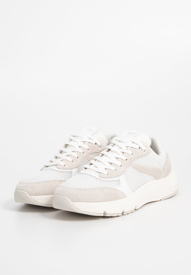 Beige-weiße Sneakers aus Mesh- und Wildledermaterial, mit runder Zehenpartie, verlängertem Sohlenbereich und strukturiertem Schaft, der ein traditionelles Schnürdesign aufweist.