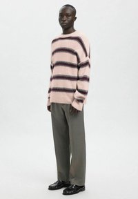 Lichtroze trui met donkerpaarse en grijze strepen. Zachte, getextureerde stof. Gecombineerd met grijze broek en zwarte loafers.