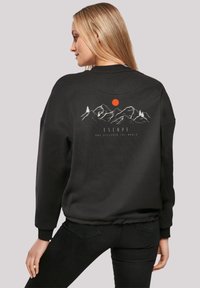 Sudadera negra con un gráfico de montaña y un sol rojo en la parte posterior. El material parece texturizado con puños y dobladillo acanalados.