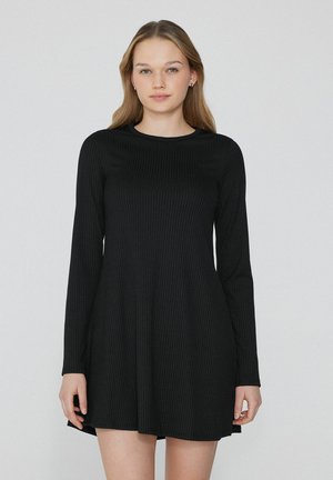 Robe noire à manches longues avec une texture côtelée, ornée d'un col rond et d'une silhouette évasée qui tombe au-dessus du genou.