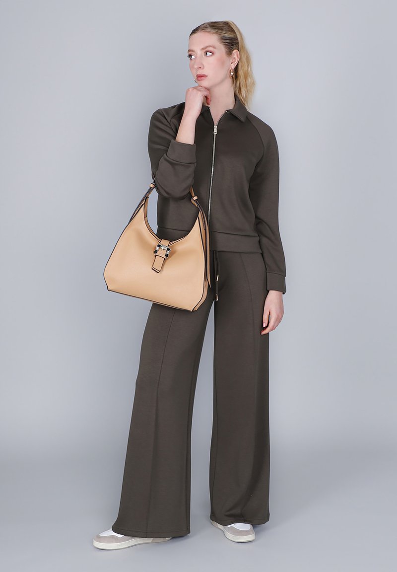 Hnědá zipová mikina a sladěné kalhoty s širokými nohavicemi z měkké tkaniny, doplněné béžovou koženou kabelkou se stříbrným akcentem.