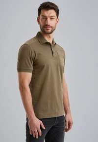 Olivengrøn polo shirt lavet af bomuld, med krave, korte ærmer og en brystlomme. Glat tekstur med let stræk.