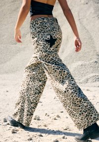 Pantaloni a gamba larga in stampa leopardata beige e nera, con un dettaglio a stella sul retro. Realizzati in un tessuto morbido con un design fluido.