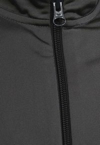 Černá mikina s kapucí na zip z texturované látky. Obsahuje výrazný zip a logo Adidas na táhlu zipu.