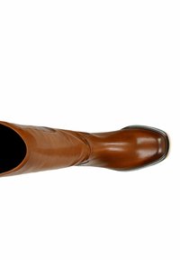 Botte montante en cuir marron avec une finition lisse, un bout arrondi et un subtil détail de couture le long de la tige. Semelle en caoutchouc noir visible.