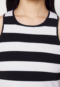 Gros plan d'une personne portant un haut sans manches côtelé à rayures horizontales noires et blanches avec un col rond.