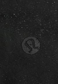 Tissu noir texturé avec des gouttes d'eau et un logo circulaire brillant avec un design abstrait stylisé au centre.