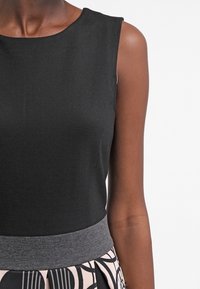 Haut sans manches noir au toucher lisse et à encolure ronde, doté d'une ceinture élastique grise et d'une jupe à motifs en dessous.