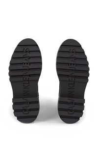 Suole di scarpe in gomma nera con profondi motivi di battistrada. Presentano un marchio in rilievo "CALVIN KLEIN JEANS" e un design della punta piatta e arrotondata.