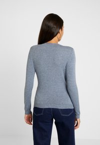 Maglione blu a maglia con scollatura rotonda e maniche lunghe. Texture morbida con orlo a coste. Abbinato a pantaloni in denim scuro.