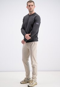 Czarna bluza z okrągłym dekoltem i ściągaczami na rękawach, w zestawieniu z beżowymi spodniami o wąskim kroju. Buty w jasnoszarym kolorze z teksturowanym wykończeniem.