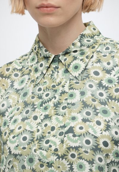 Close-up of a person wearing a collared shirt with a green and white floral pattern resembling sunflowers.