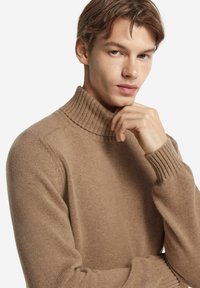 Stickad polotröja i ljusbrun med ribbat krage och mudd, som har en mjuk textur och figurnära design.