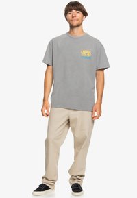 Gray cotton t-shirt with a front graphic design featuring a wave and swirl pattern in yellow and blue. Loose fit, crew neck design.