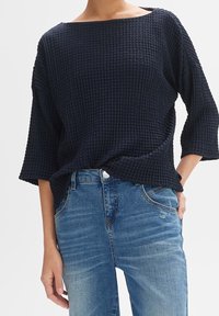 Marinblå stickad topp med ett strukturerat mönster, bred båthals och trekvartsärmar, kombinerad med ljusblå denimjeans.