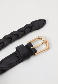 Czarny pleciony skórzany pasek o gładkim wykończeniu. Posiada złotą metalową klamrę oraz dekoracyjny skórzany koniec z przeszyciem.