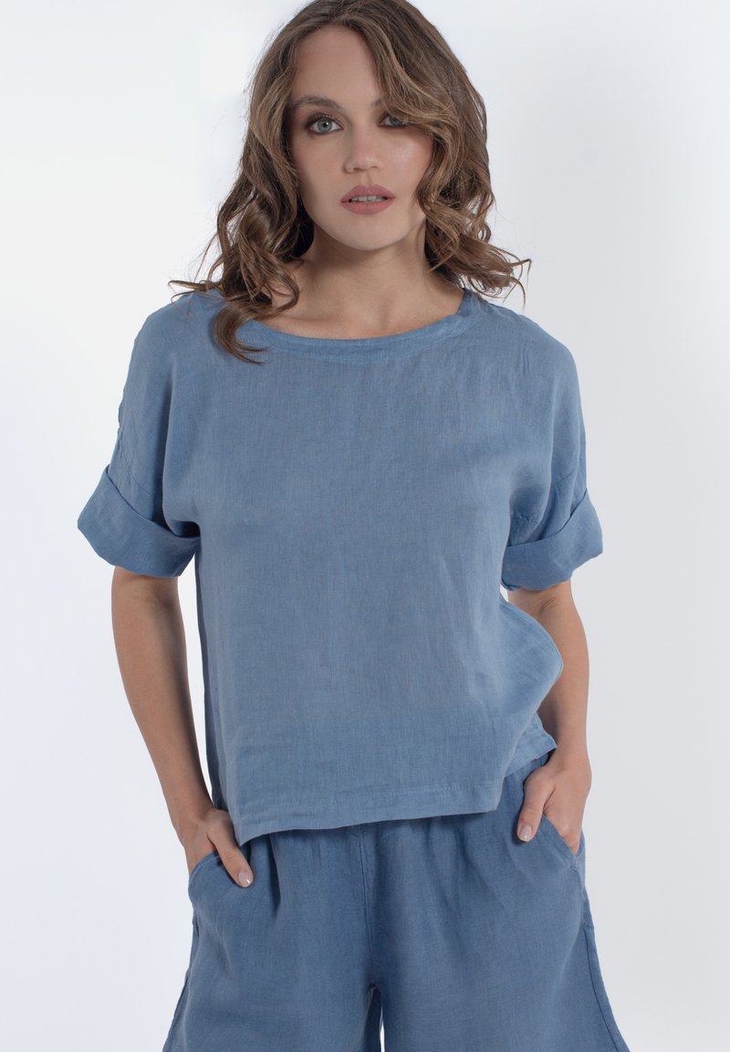 Top in lino azzurro chiaro con maniche corte arrotolate e collo a barca. Presenta una vestibilità morbida e una texture liscia. Abbinato a pantaloni coordinati.