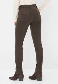 Jeans marroni slim fit con vita alta, tasche laterali, tasche posteriori e una texture liscia, abbinati a stivaletti con tacco marroni.