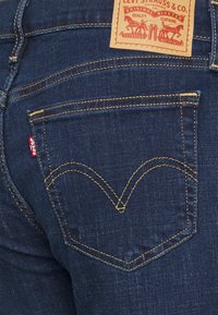 Mörkblå denimjeans med en klassisk femfickdesign, kontrasterande guldstickning och en läderlapp med texten "Levi Strauss & Co." på midjan.