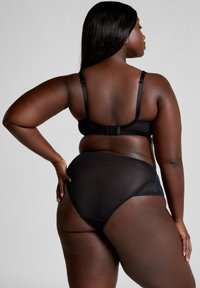 Zwart lingerie set met een zachte beha met verstelbare bandjes en een haaksluiting, aangevuld met doorschijnende, taillehoge slips met kanten accenten.