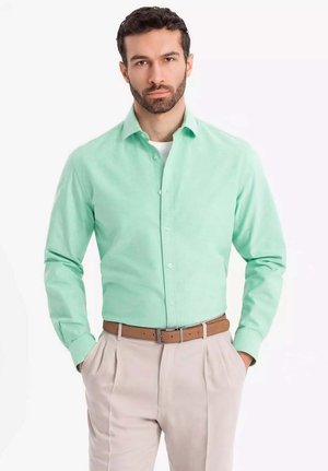 Light green button-up shirt with long sleeves, collared design, paired with beige pleated trousers and a brown belt.