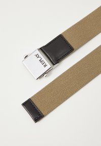 Cintura in tela khaki con accento in pelle nera; presenta una fibbia argentata riportante la scritta "REPLAY". Tessuto testurizzato e design robusto.