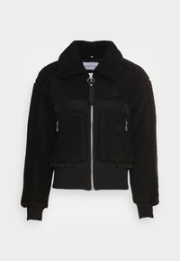 Czarna kurtka bombowca z teksturą sztucznego baranka, z przodem na zamek błyskawiczny oraz dwoma kieszeniami na zamek. Szczegóły z prążkowanym wykończeniem przy mankietach i dolnej krawędzi.