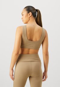 Beige sports bra with a wide neckline and thick straps, paired with matching high-waisted leggings, both featuring a soft, stretchy material.