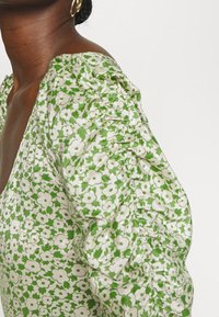 Green floral blouse featuring puffed sleeves, made of lightweight fabric with a white flower pattern and gathering details along the sleeves.