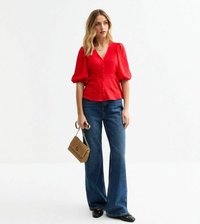 Blouse rouge à manches courtes avec fermeture à boutons et tissu texturé, associée à un jean flare noir. Petit sac à main tissé et chaussures noires.