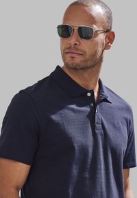 Marineblaues Polohemd mit Kragen, kurzen Ärmeln und Knopfleiste mit zwei Knöpfen. Verfügt über eine dezente Textur und ein kleines Logo auf der linken Seite.