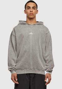 Grå oversized hettegenser laget av mykt stoff, med en frontlomme, snøring på hetten og hvit tekst "TÆNK FORSKELLIG." på brystet.