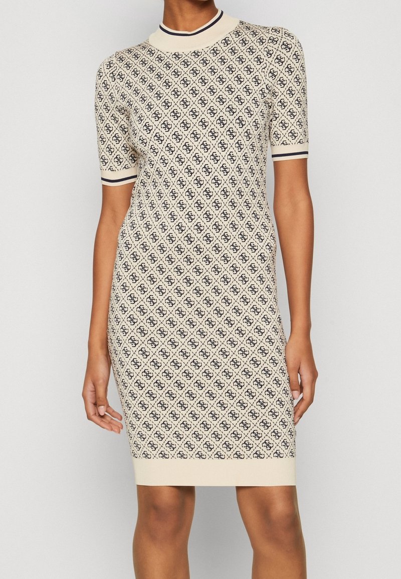 Femme portant une robe en maille crème à manches courtes avec un motif losange noir et une bordure rayée au col et aux manches.