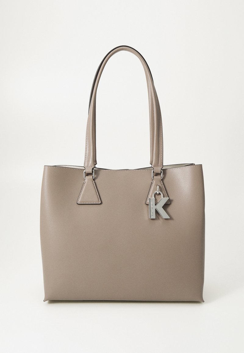 Sac cabas en cuir taupe avec double poignées et charm en forme de lettre "K" argentée suspendu près de l'attache de la poignée droite en haut.