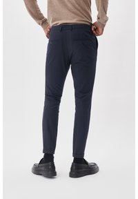 Marina slim-fit byxor tillverkade av ett glatt material, med en medelhög midja, två bakfickor och uppvikta fållar. Svarta slip-on skor.