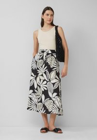 Jupe maxi à imprimé floral en noir et blanc avec une taille à cordon. Associée à un débardeur beige et des sandales noires à glissière.