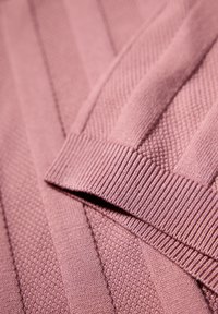 Jasnoróżowa dzianina z teksturowanymi wzorami, z prążkowanymi krawędziami i ukośnymi liniami, tworzącymi warstwowy wygląd.