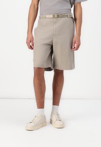 Beige bomullsshorts med ett bälte, med en avslappnad passform, sidofickor och en platt frontdesign. Bärs med vita sneakers och strumpor.