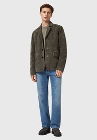 Giacca in suede grigia con rever a punta, due tasche frontali e tre bottoni, abbinata a jeans dritti blu chiaro e scarpe nere.