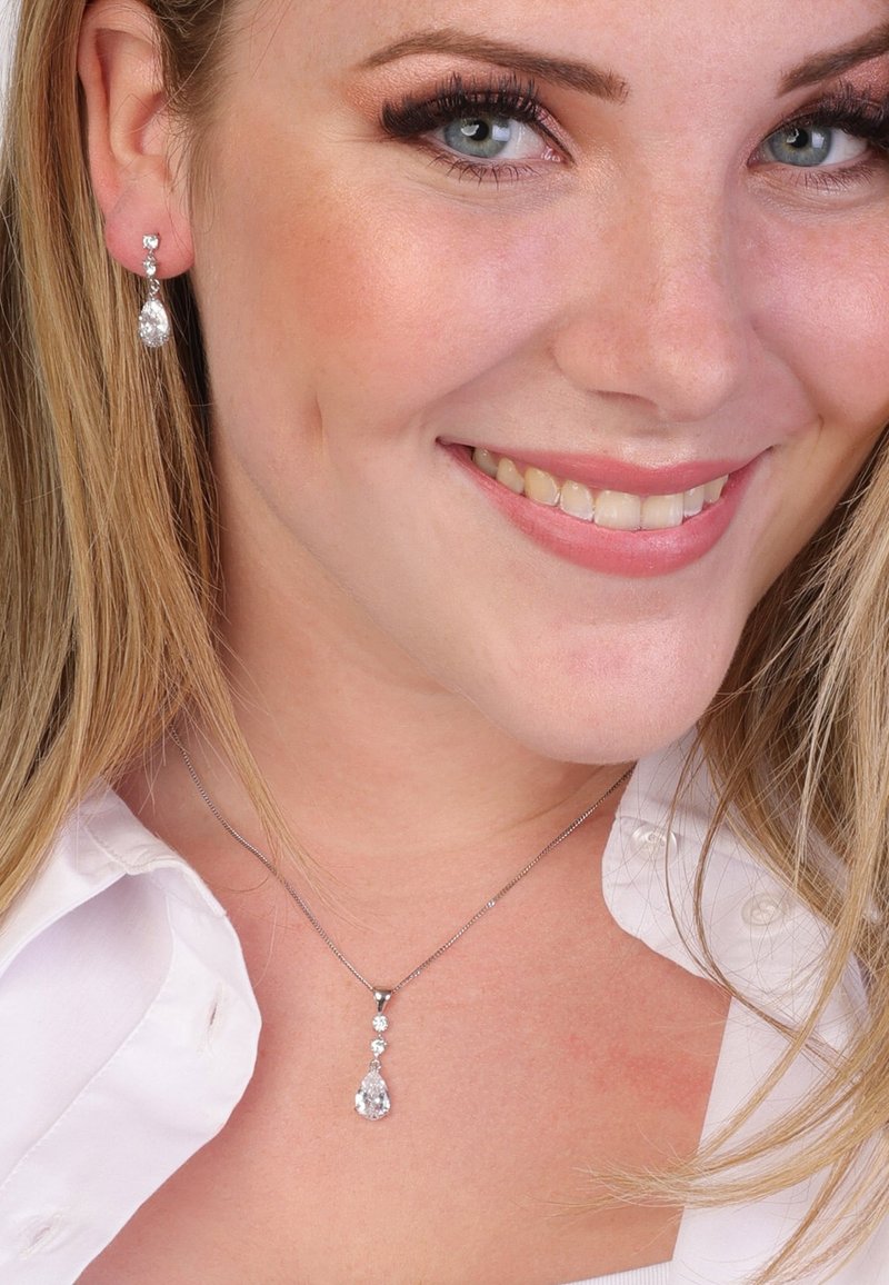 Zilveren ketting met een druppelvormige hanger en drie kleine accenten; bijpassende hangoorbellen hebben een druppelontwerp. Beide zijn versierd met heldere edelstenen.