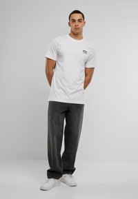 Witte katoen T-shirt met korte mouwen en zwarte grafische tekst op de borst, gecombineerd met donkergrijze losse broek en witte sneakers.