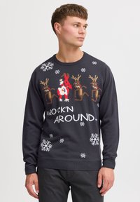Dunkelgrauer Pullover mit Rentier- und Schneemann-Muster, weißen Schneeflocken und dem Text "ROCK'N AROUND" in fetter Schrift. Stricktextur, lange Ärmel.
