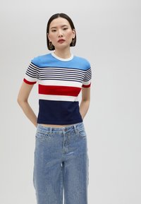 Randig kortärmad stickad topp i blått, vitt, rött och marinblått; slim fit; rund hals; har olika stripbredder. Bärs med hög midja denim.