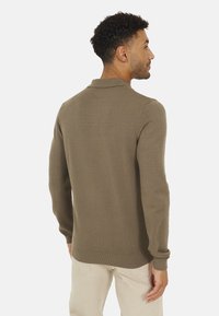 Maglione polo a maglia marrone con colletto e polsini a costine, che presenta una fine texture. Il design presenta una silhouette minimalista e aderente.