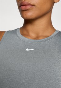 Szary t-shirt Nike bez rękawów z okrągłym dekoltem i subtelną teksturowaną powierzchnią, z małym białym logo na klatce piersiowej.